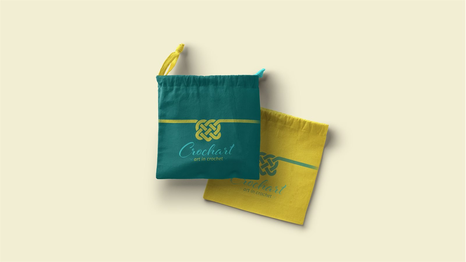 Duas necessaires de tecido com cordão, uma verde-petróleo e outra amarela, estampadas com o nó e a assinatura da Crochart