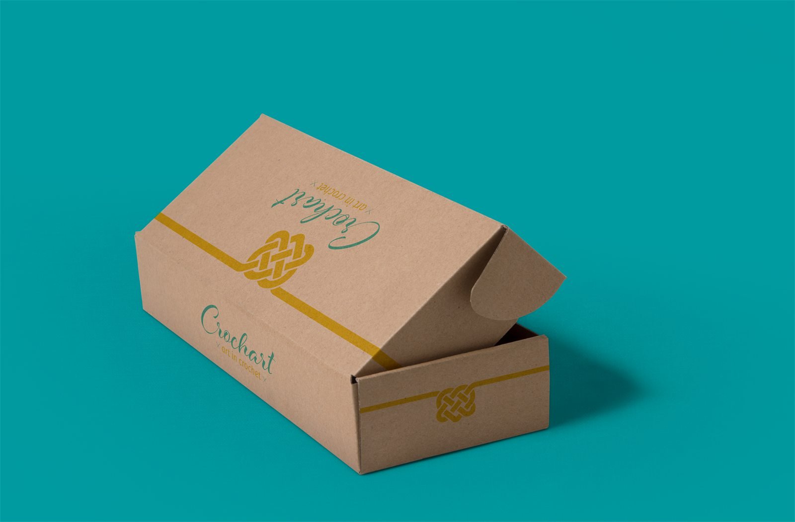 Caixa de papel kraft entreaberta, com a assinatura da Crochart e o fio amarelo com o nó contornando a tampa, sobre fundo verde-água