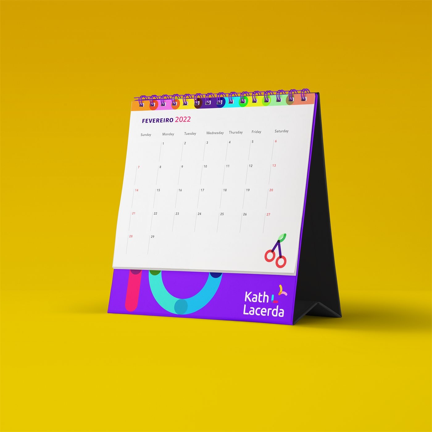 Calendário de mesa aberto em fevereiro de 2022, com cerejas ilustradas e a assinatura Kath Lacerda, sobre fundo amarelo