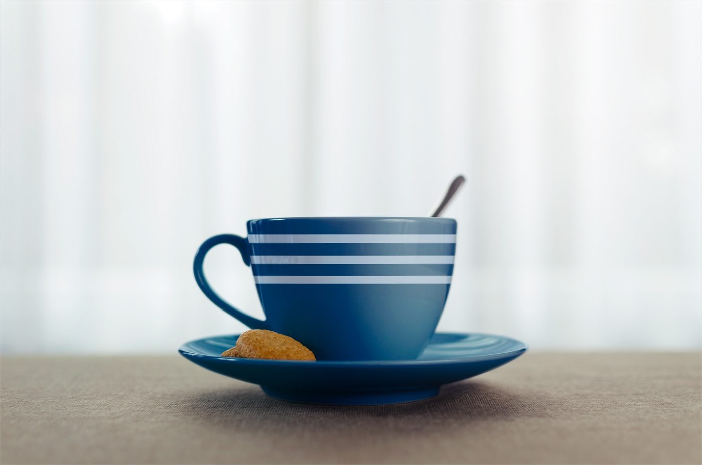 Xícara azul com as faixas brancas da marca, sobre o pires com um biscoito