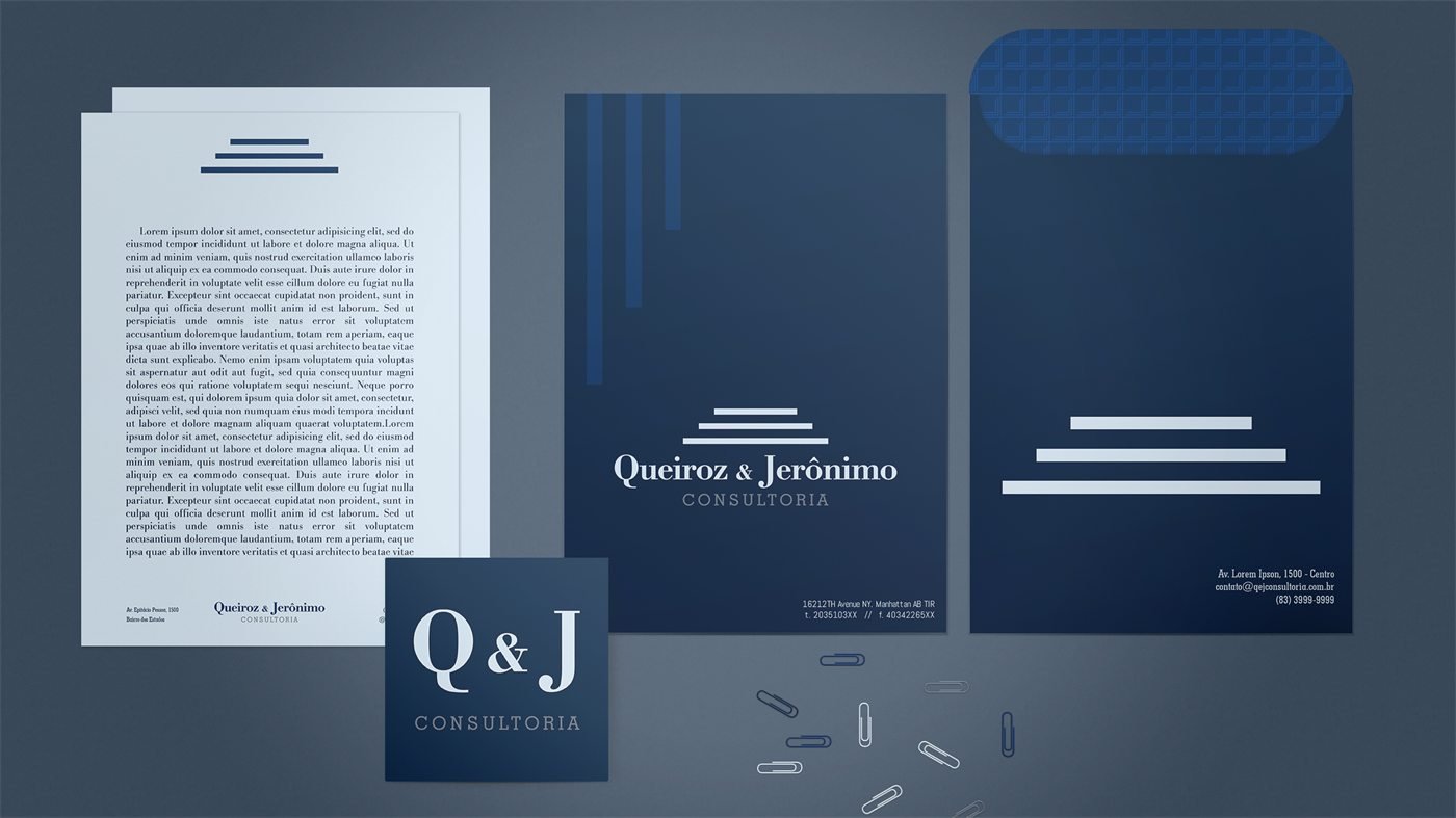 Papel timbrado, pasta, envelope e cartão Q&J Consultoria sobre fundo azul, com clipes espalhados