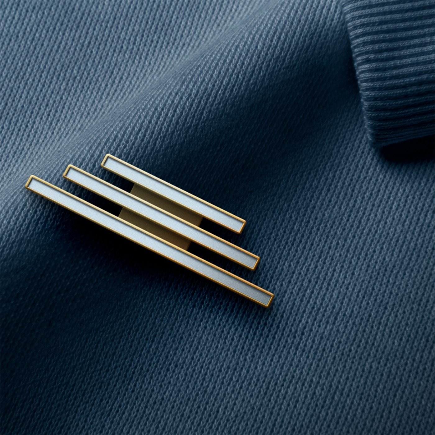 Pin metálico com as três barras da escada, em dourado e esmalte branco, preso num tecido azul