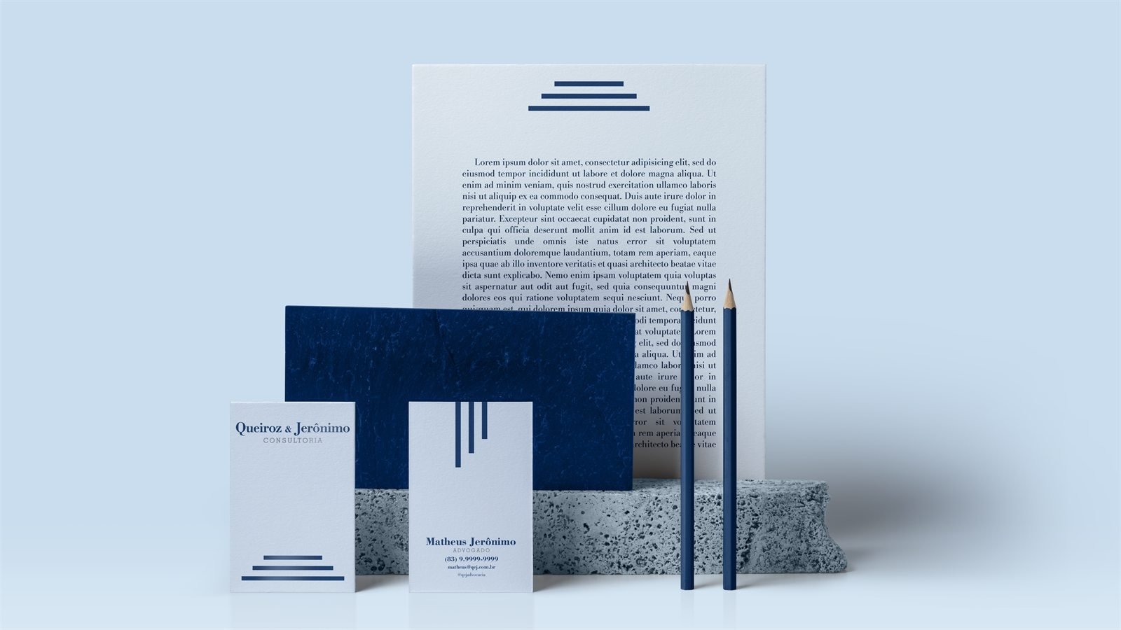 Papel timbrado com o símbolo da escada, envelope azul texturizado, cartões de visita e dois lápis azuis sobre uma pedra de granito