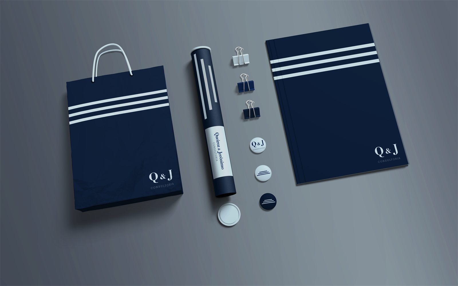 Kit de escritório em azul-marinho com as faixas brancas da marca: sacola e caderno com Q&J, tubo, clipes e bottons