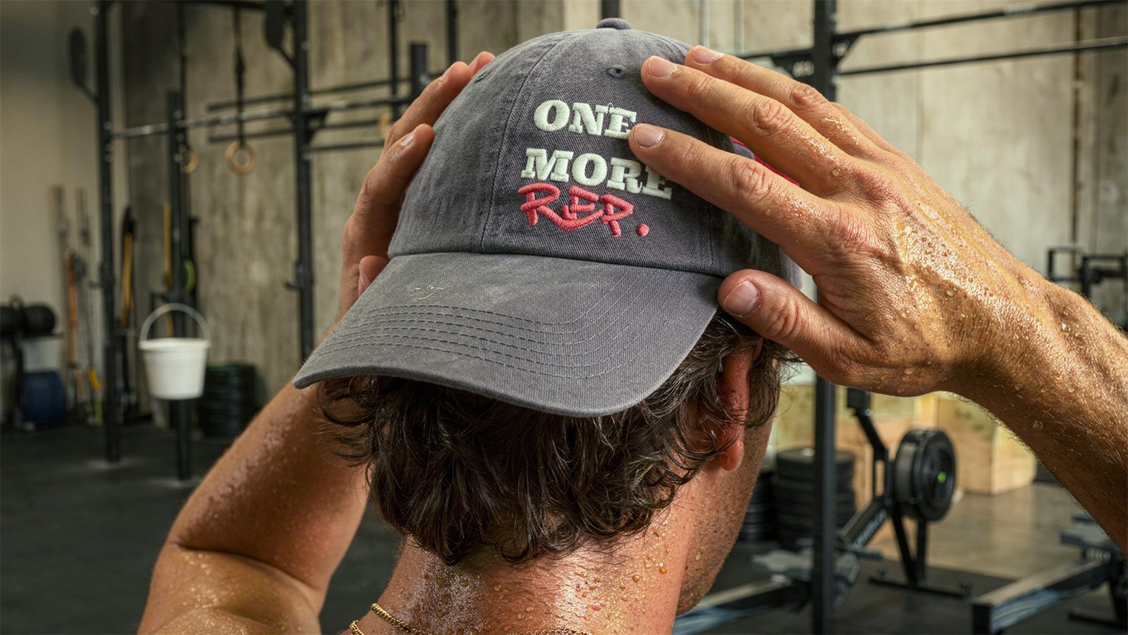 Atleta suado ajeita com as duas mãos o boné cinza bordado One More Rep, no box