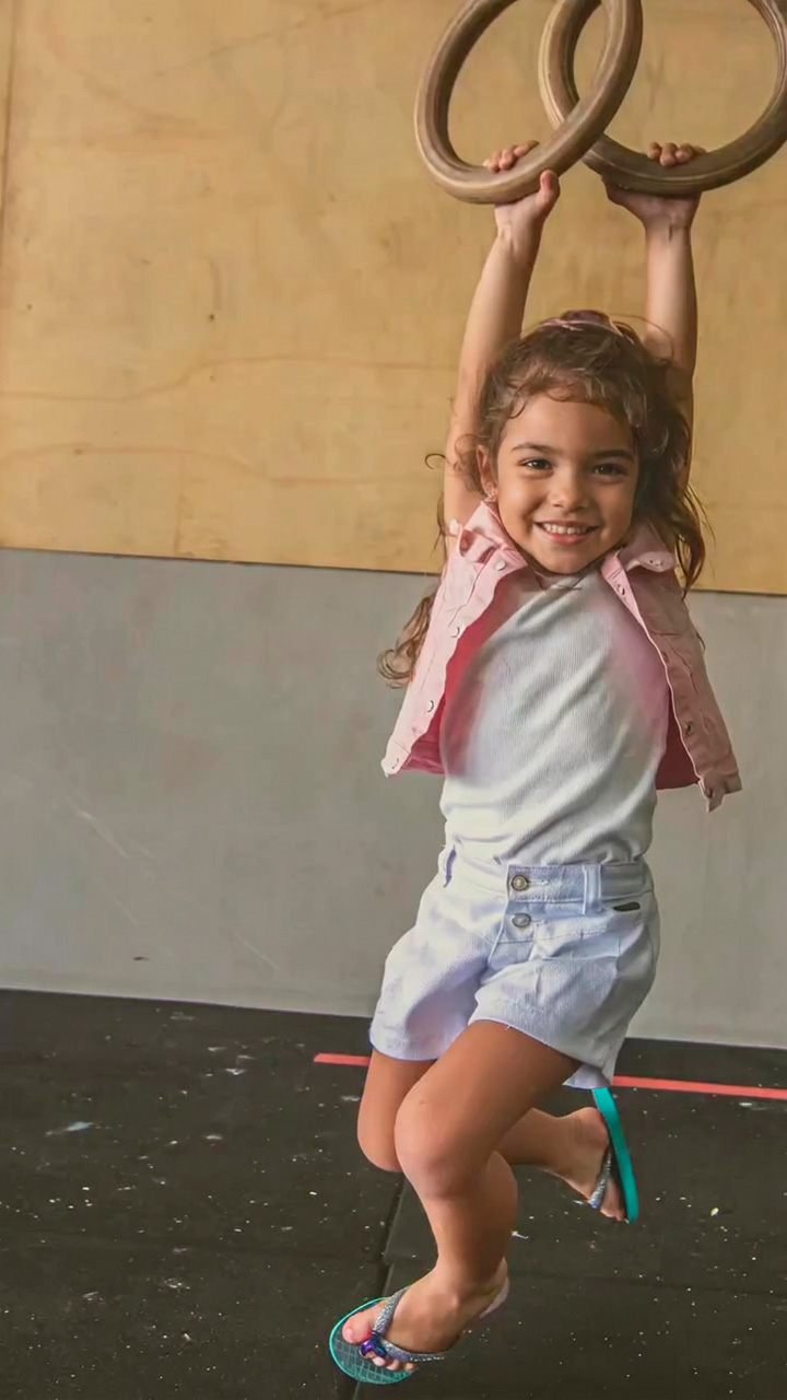 Menina sorridente pendurada nas argolas de ginástica do box